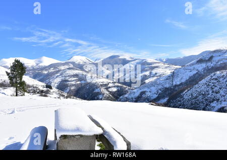 Paesaggio invernale con montagne innevate e il punto di vista di pietra con tavolo e panche coperte di neve. Lugo, Galizia, Spagna. Foto Stock