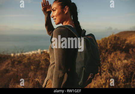 Donna escursionista guardando a distanza con la mano sopra gli occhi. Femmina con zaino in paese a piedi alla ricerca di distanza a una vista. Foto Stock