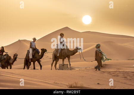 Linea di persone che viaggiano da cammello sotto il caldo sole, Merzouga, Marocco Sahara Desert - Erg Chabbi dune Foto Stock