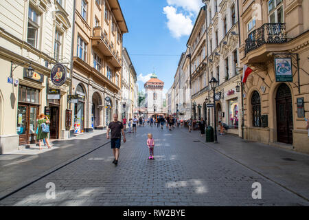 Bambina corse su uno scooter lungo le strade di ciottoli della Piazza del Mercato di Cracovia-w Città Vecchia con Brama Florianska, City Gate di parete, dietro di loro Foto Stock