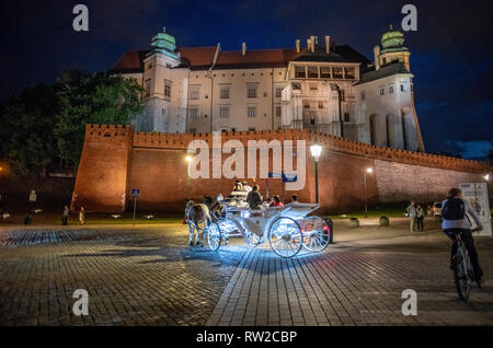 L'accensione di un carro trainato da cavalli porta i passeggeri lungo la strada acciottolata con il Castello Reale di Wawel aleggiano sopra di loro, Kraków-w, Piccola Polonia Voivo Foto Stock