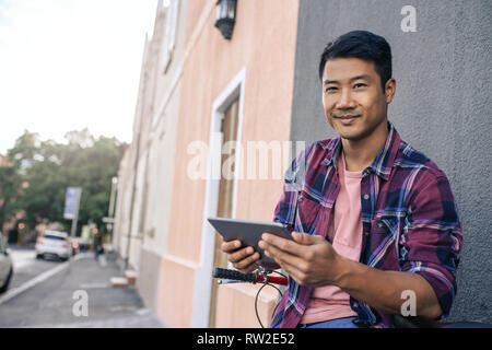 Sorridente giovane uomo seduto sulla sua moto utilizzando un tablet Foto Stock