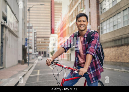 Uomo sorridente in piedi con la sua bicicletta su una strada di città Foto Stock