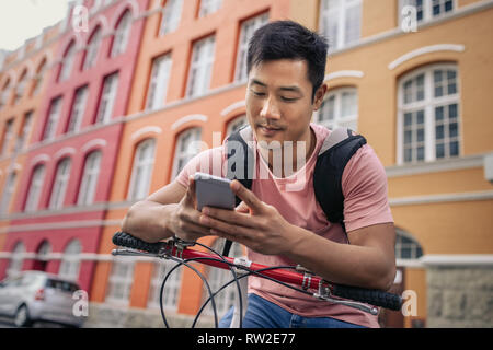 Giovane uomo seduto sulla sua bicicletta inviando un messaggio di testo Foto Stock