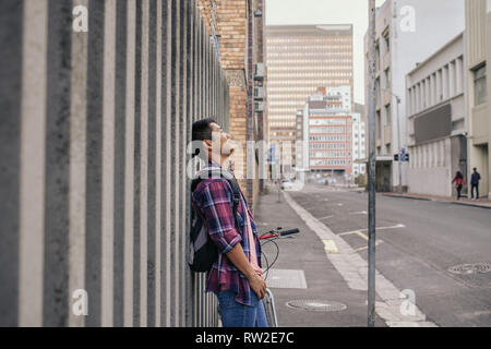 Giovane uomo con gli occhi chiusi appoggiato contro una parete della città Foto Stock