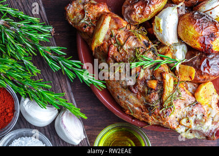 Deliziosi e gustosi arrosto di maiale con spezie e patate (pepe nero, olio d'oliva, aglio, rosmarino fresco, sale). Sul legno scuro backgr Foto Stock