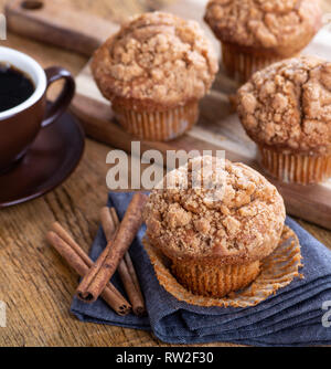 Muffin alla cannella e bastoni su un tovagliolo blu con tazza di caffè e muffin in background Foto Stock