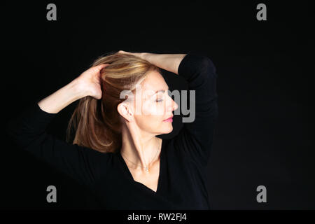 Close up studio ritratto di una bella donna in abito nero su sfondo nero Foto Stock