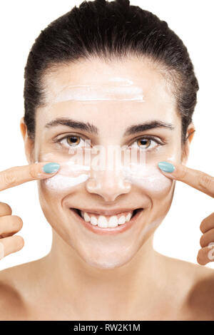 Bella ragazza mettendo la crema sul suo viso con un sorriso Foto Stock