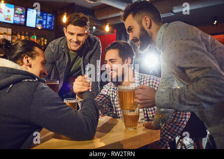 Amici fare divertimento di wrestling del braccio in un pub. Foto Stock