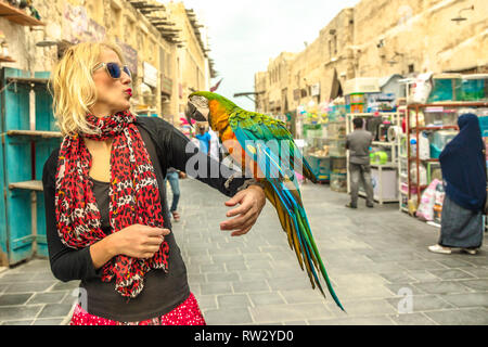 Donna felice baci un pappagallo a Bird Souq all'interno Souq Waqif, il mercato vecchio e di attrazione turistica in Al Souq District, Doha city centre, in Qatar Foto Stock