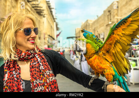 Ritratto di donna interagisce con un pappagallo con ali aperte al Souq di uccelli all'interno Souq Waqif, il vecchio mercato di attrazione turistica nel centro di Doha, in Qatar Foto Stock