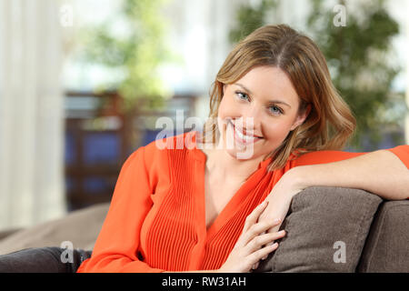 Vista frontale il ritratto di una bella casa in posa guardando la telecamera seduta su un divano nel salotto di casa Foto Stock