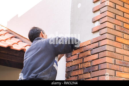 Lavoratore mettendo i mattoni rossi sui muri di casa Foto Stock
