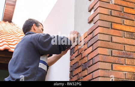 Lavoratore mettendo i mattoni rossi sui muri di casa Foto Stock