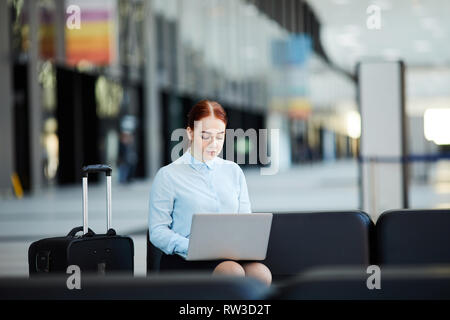 Ritratto di giovane imprenditrice utilizzando computer portatile mentre si è in attesa in aeroporto lobby, spazio di copia Foto Stock