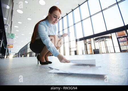 A piena lunghezza Ritratto di giovane imprenditrice di prelevare documenti dal pavimento in office hall, spazio di copia Foto Stock