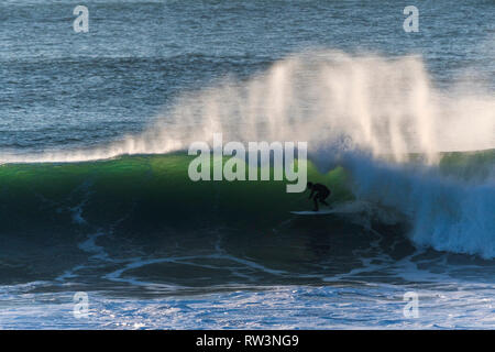 Un surfista in sella a una grande onda al largo della costa di Newquay Cornwall. Foto Stock