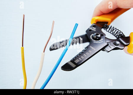 Elettricista utilizza il filo tagliente di estrazione per rimuovere di isolamento dalla punta di ciascuno dei fili durante il cablaggio elettrico dei servizi, close-up. Foto Stock