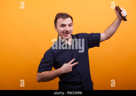 Felice giovane uomo che mostra segno di vittoria e tenendo il telefono cellulare su giallo backdround. Funny giovane uomo Foto Stock
