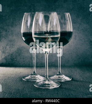Un bicchiere di vino bianco di fronte a due bicchieri di vino rosso Foto Stock