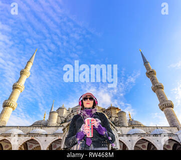 Bella donna di cappello con caffè da asporto occhiali da sole,cuffie sta al Cortile della moschea di Sultanahmet o la Moschea Blu a Istanbul, Turchia Foto Stock