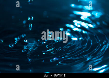 Splash di gocce di acqua su una superficie di acqua colorata con inchiostro celesti. Concetto di purezza, pulizia e conservazione delle risorse non rinnovabili. Abstr Foto Stock