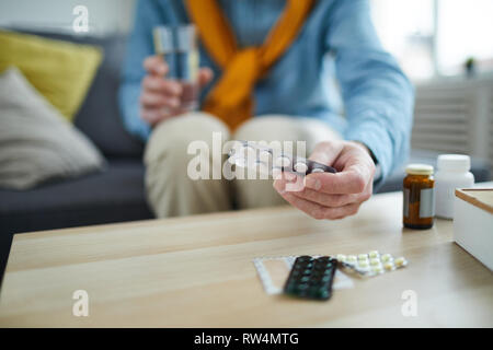 Primo piano di un irriconoscibile uomo senior assunzione di pillole e medicinali fuori dalla tavola a casa, spazio di copia Foto Stock