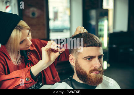 Client durante la rasatura della barba in barberia. Barbiere femmina al salone. La parità tra i sessi. Donna nel maschio professione. Foto Stock