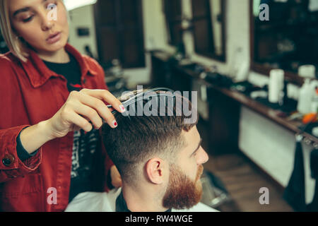 Client durante la rasatura della barba in barberia. Barbiere femmina al salone. La parità tra i sessi. Donna nel maschio professione. Foto Stock