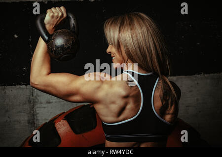 Giovani muscolare di bella donna sta facendo esercizio con kettlebell in palestra. Foto Stock