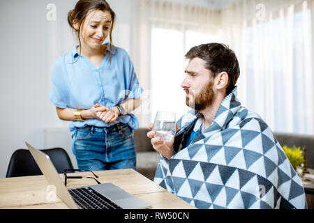 Giovane donna facendo attenzione a dare qualche medicina per un uomo la sensazione di malessere coperti con coperta a casa Foto Stock