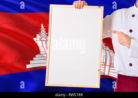 Lo Chef cambogiano azienda lavagna vuota menu sulla Cambogia bandiera dello sfondo. Cuocere indossano uniformi di spazio di puntamento per il testo. Foto Stock