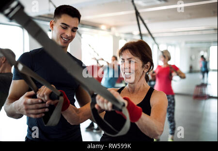 Un gruppo di allegro anziani in palestra con un giovane allenatore di fare esercizio con TRX. Foto Stock