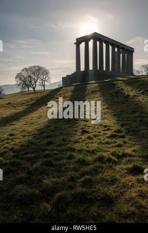 Cerca fino alla silhouette del Monumento Nazionale di Scozia con il sole che splende da dietro di esso su Calton Hill a Edimburgo, Scozia Foto Stock