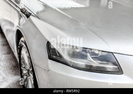 Argento auto luce anteriore lavato in self service autolavaggi. Dettaglio di acqua corrente a getto di spruzzatura sulla copertura in vetro. Foto Stock