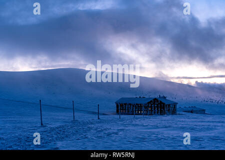 Cabina di montagna con una luce calda in windows incandescente all'imbrunire circondato dal paesaggio di neve. Foto Stock