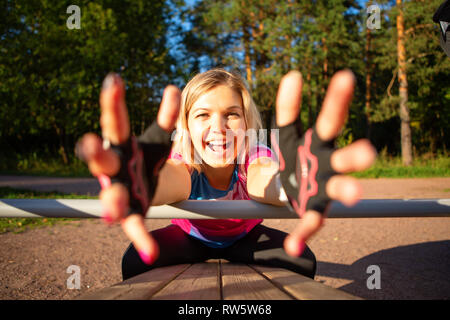 Atleta ragazza tirando le mani avanti esercita a panca in legno nel parco sulla mattina d'estate Foto Stock