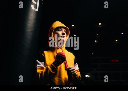 Sportive boxer in felpa gialla tira bende rosse sulle sue mani su sfondo nero Foto Stock