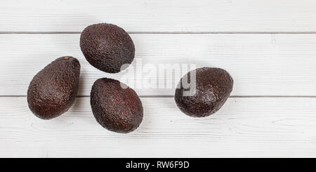 Vista dall'alto in basso, quattro mature brown avocadi su lavagne bianche desk. Foto Stock