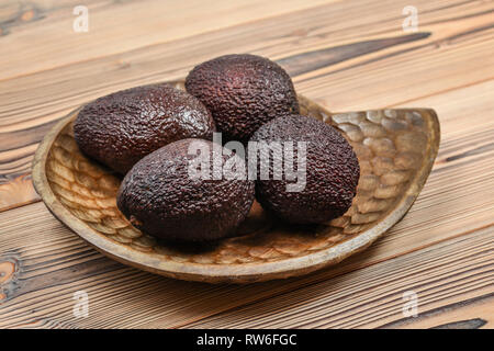 Quattro mature brown avocadi su legno scolpito ciotola. Foto Stock