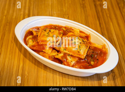 Freschi cotti i ravioli in salsa di pomodoro in un piatto bianco su un legno tagliere. Foto Stock