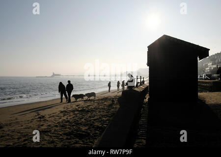 Cani e persone a piedi lungo la spiaggia di Sandown in una pigra domenica pomeriggio si stagliano in bright nebuloso sole invernale. Foto Stock