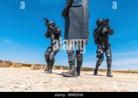 Basso angolo vista di SWAT speciali di polizia costringe gli operatori di nascondersi dietro la protezione balistica. Foto Stock