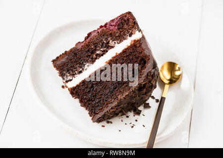 Fetta di torta al cioccolato con crema la glassa sulla piastra bianca e dorata cucchiaio da tè per mangiare. Primo piano Foto Stock