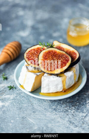 Camembert o formaggio brie con fichi, miele blu su sfondo concete. Messa a fuoco selettiva Foto Stock