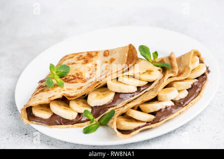 Il cioccolato noccioletta e riempito di banana crepes sulla piastra bianca. Isolato. Primo piano Foto Stock