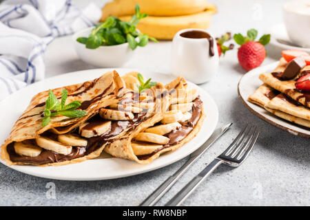 Il cioccolato noccioletta e riempito di banana crepes sulla piastra. Gustose crepes o blini con salsa dolce e frutta. Primo piano Foto Stock