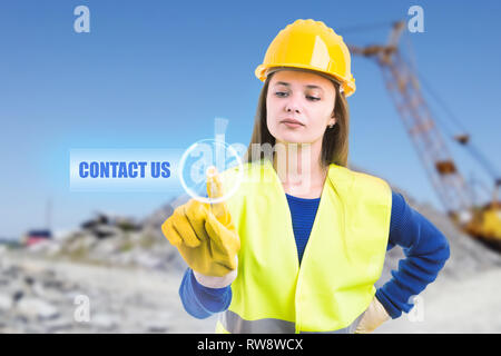 Giovane donna builder di toccare con il dito indice contattaci pulsante su schermo trasparente come il futuristico concetto di comunicazione Foto Stock