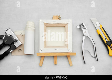 Artista tela su cavalletto in legno, tela in rotolo, canvas pilers barella, il coltello e la pistola di fiocco su sfondo marmo. Pittori forniture. Vista dall'alto. Foto Stock